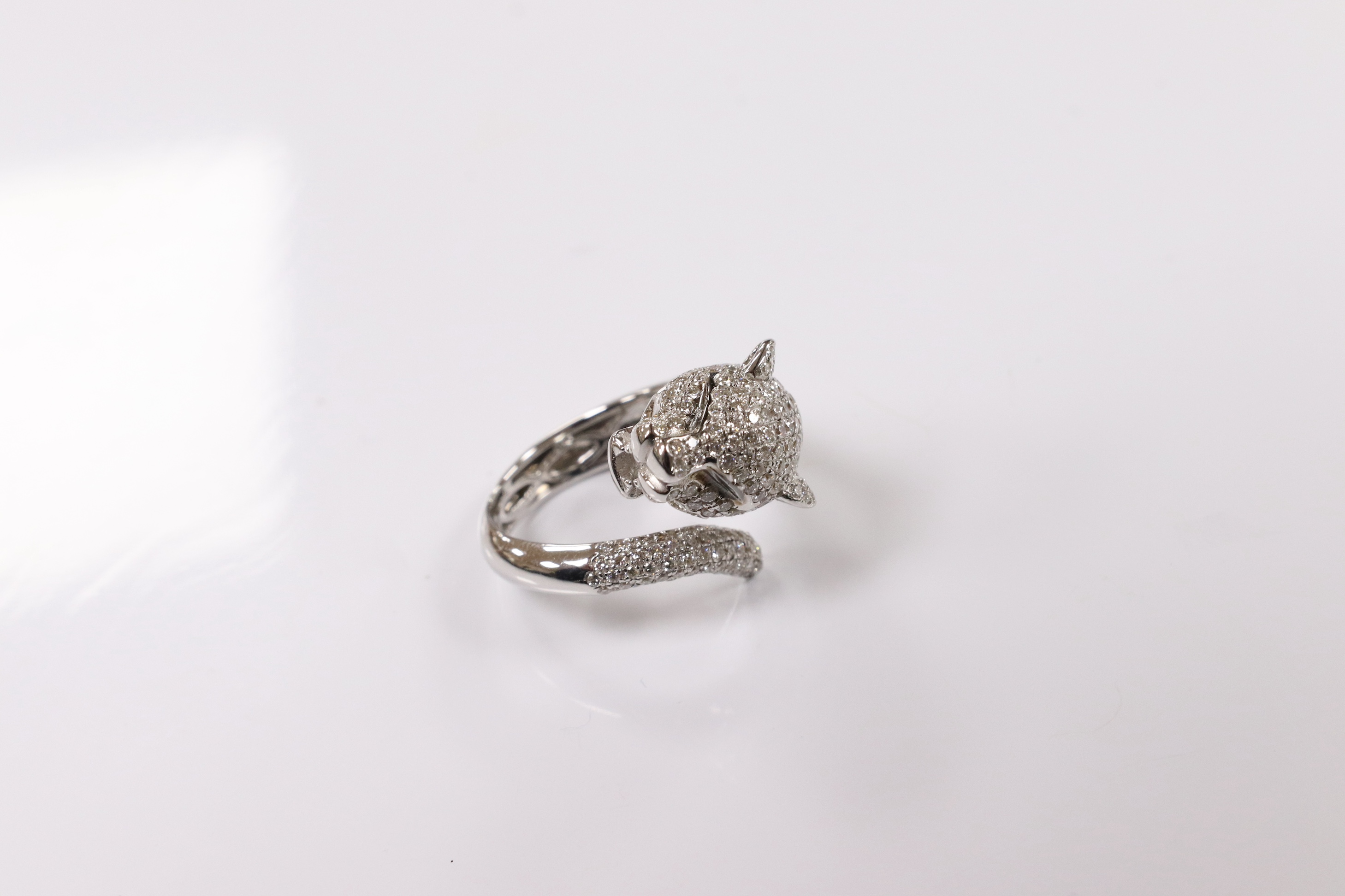 A modern Cartier style 18k white metal and pave set diamond chip dress ring, modelled as the head and tail of a leopard, size M, gross 9 grams. Condition - good